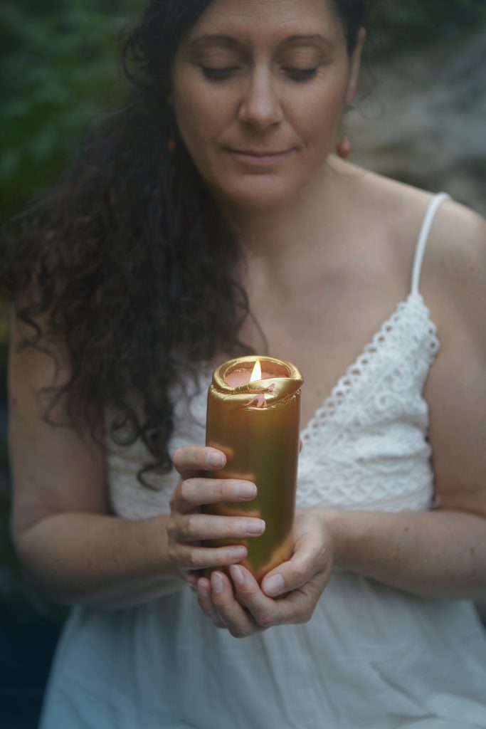 Femme en robe blanche, tenant une bougie dorée. Elle sourit à la vie.