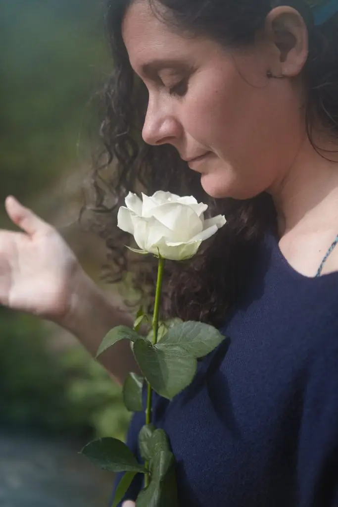 Une femme respirant le parfum d'une rose blanche. Elle est sereine et en paix