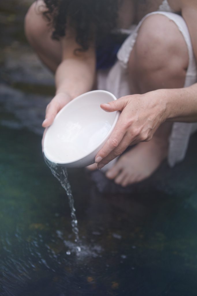 Femme accroupie au bord de l'eau, elle verse de l'eau. Confiance et paix. Amour de soi