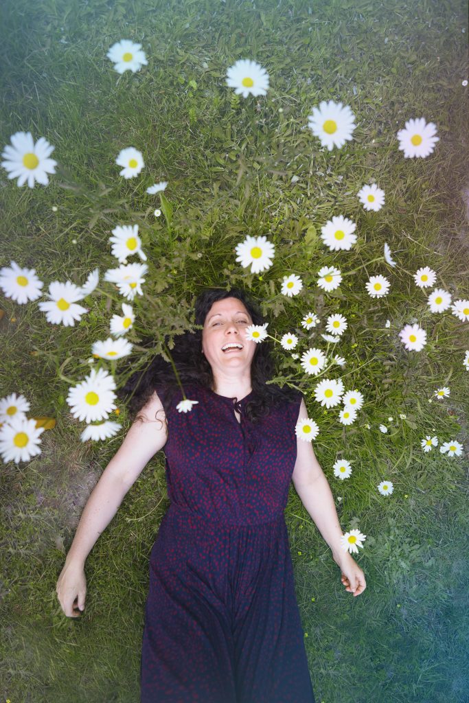 Femme allongée dans un champ de marguerites. Elle rigole et se sent confiante, sereine pleine d'élan et de joie. Harmonie Intérieure.